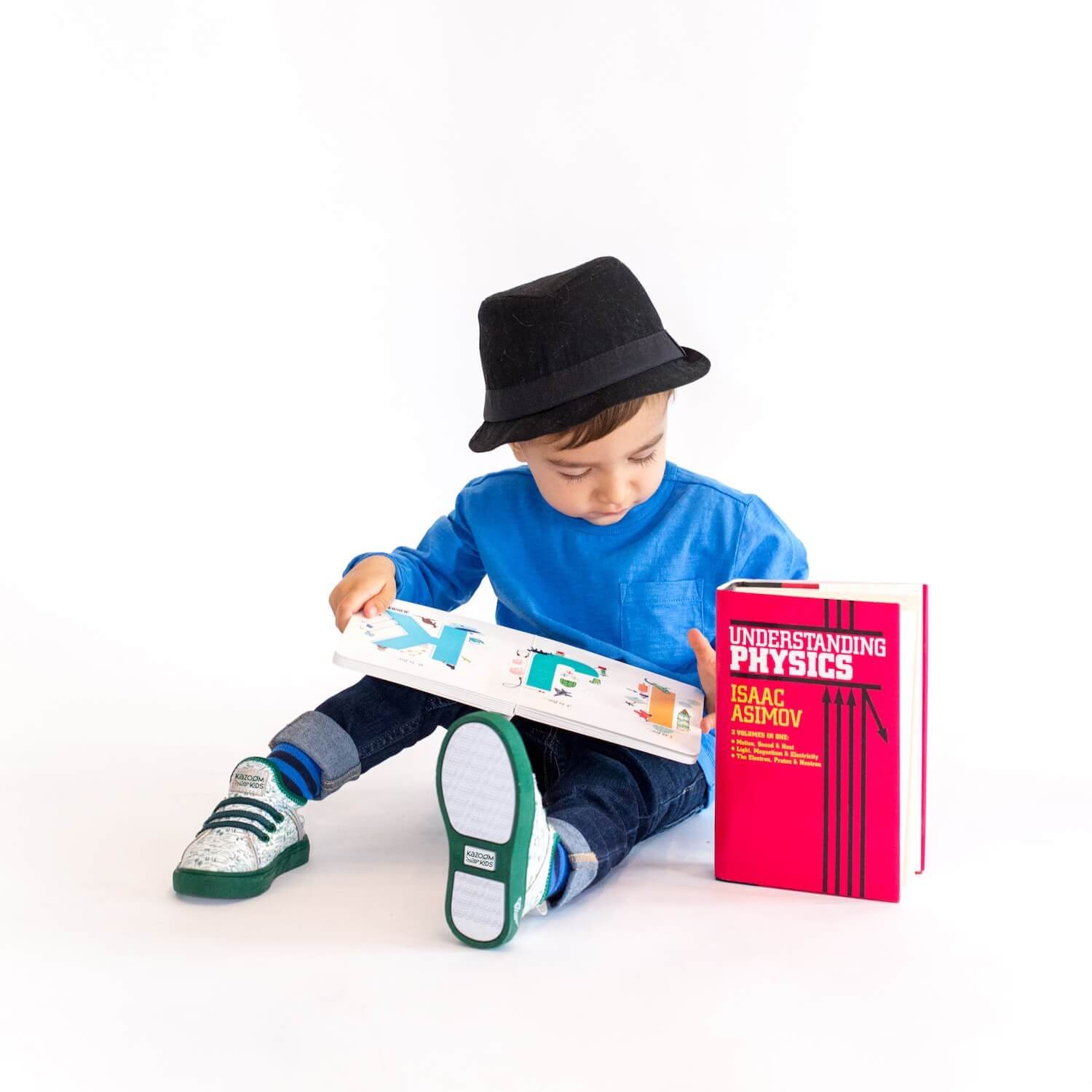 Dinosaur Sneakers being worn by Toddler - in Green Dinos sneaker pattern while reading physics book